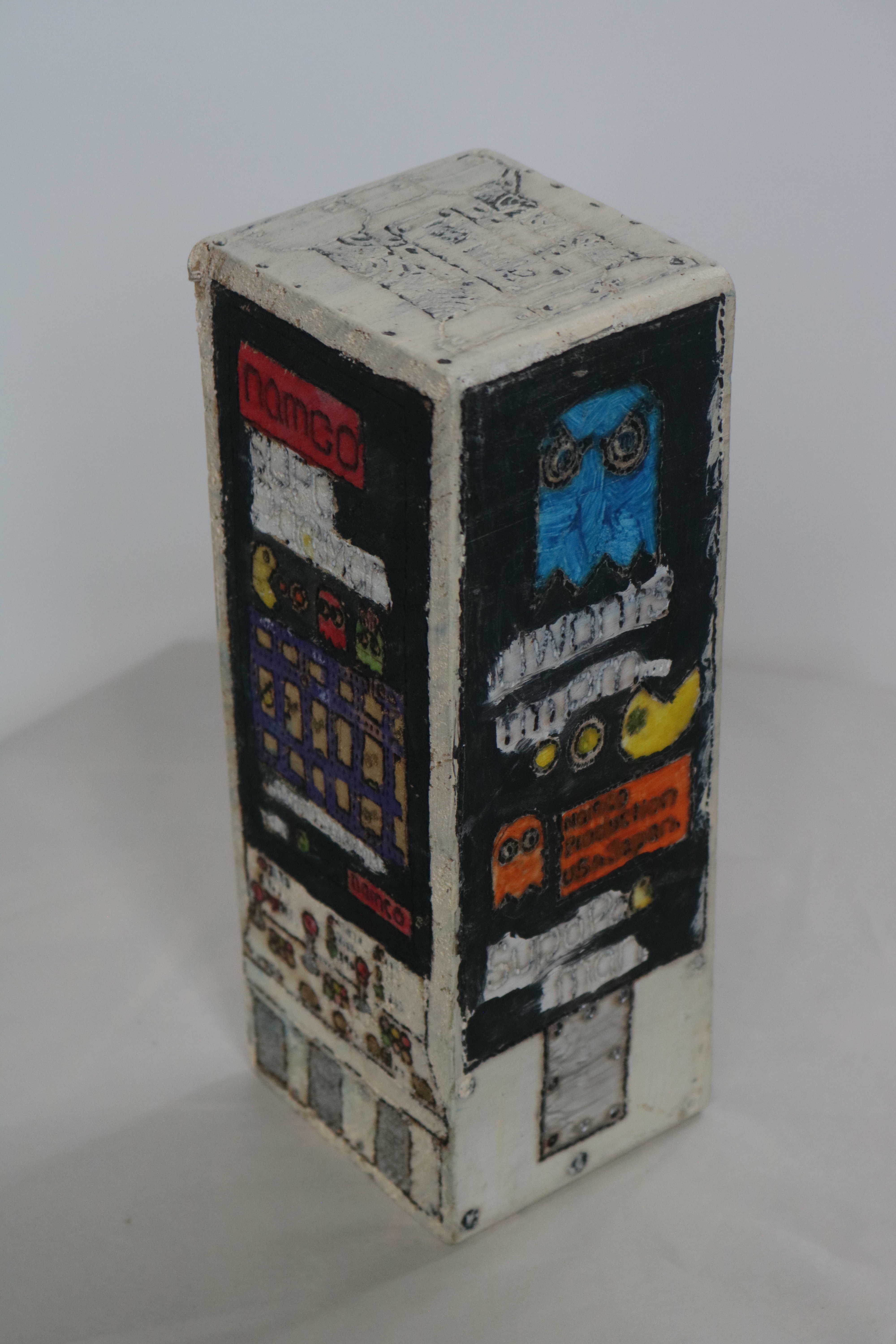 A wooden block with the word Namco on top. There are shaped of the bitton and joystick painted on. there are classic pacman ghosts, and of course pacman himself.