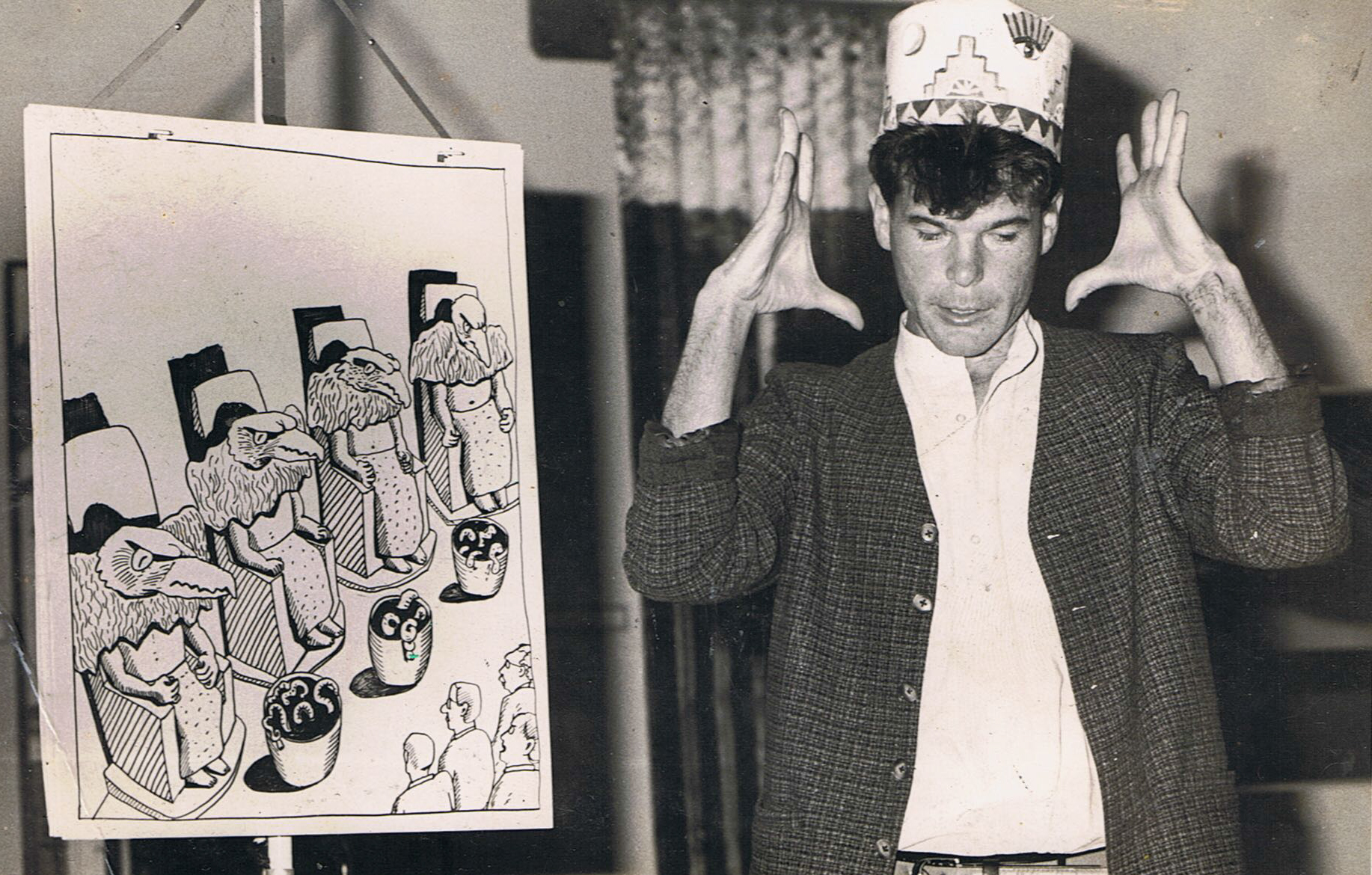 Gerard Crewdson tellinga tale with a paper crown on his head and a painting to his right.