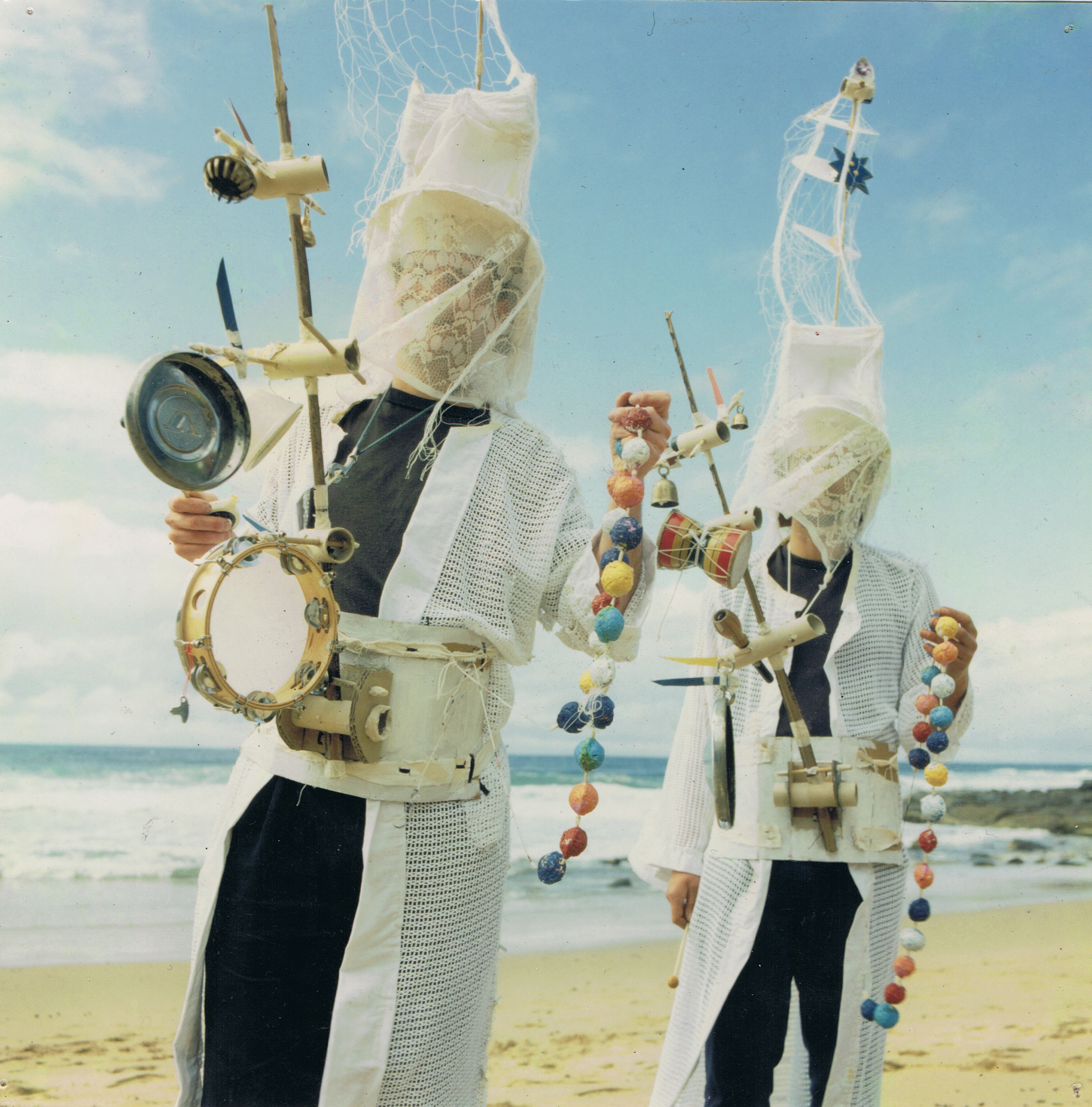 two performers wearing masks and carrying percussion trees.