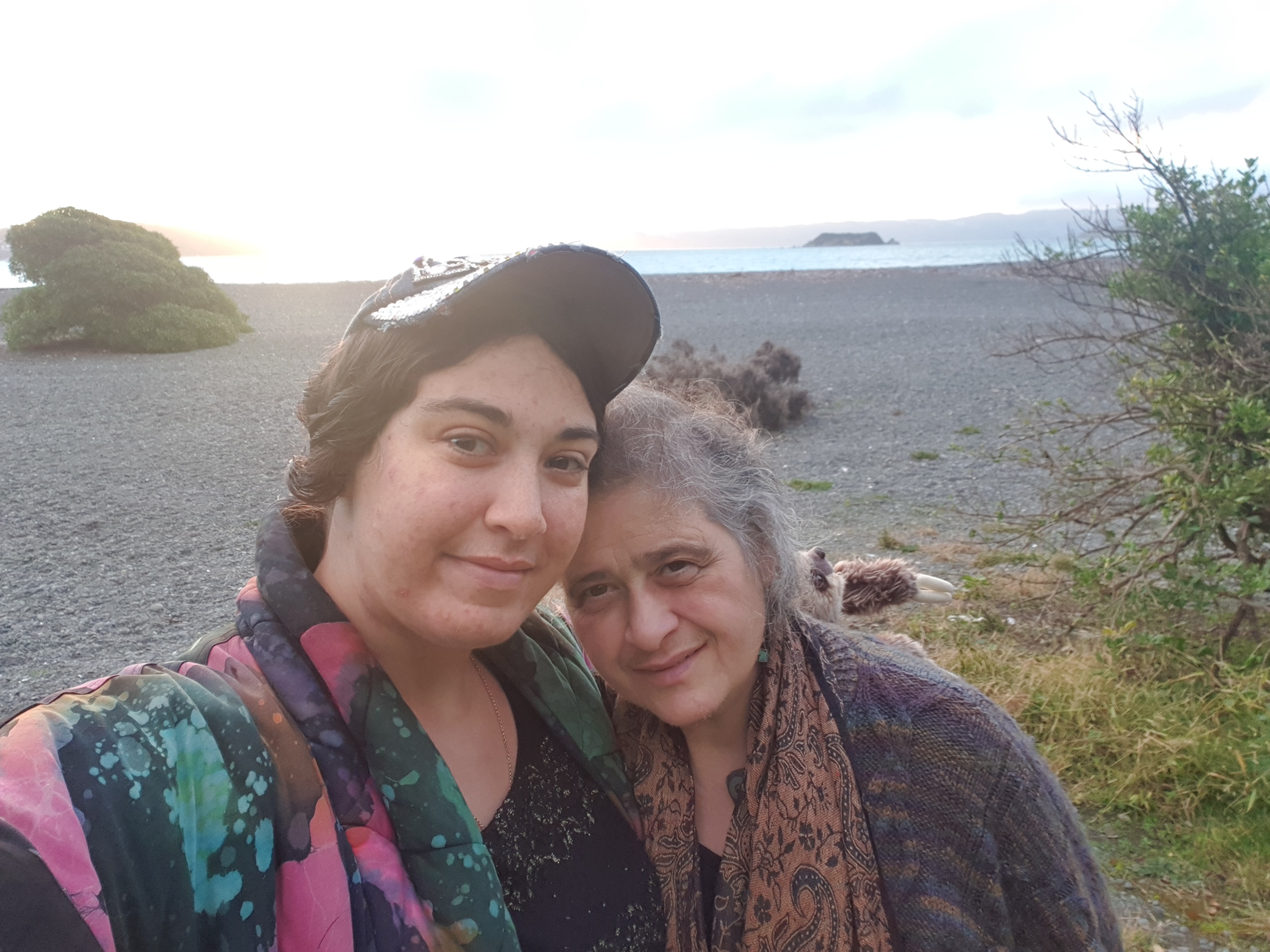 Marika and Athena on a stony beach, they have their arms around each other and their heads are touching in happy familiarity