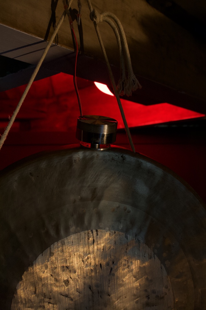 The top of a gong. It is tied to a steel girder. It has something metal wired to the top to create the resonances