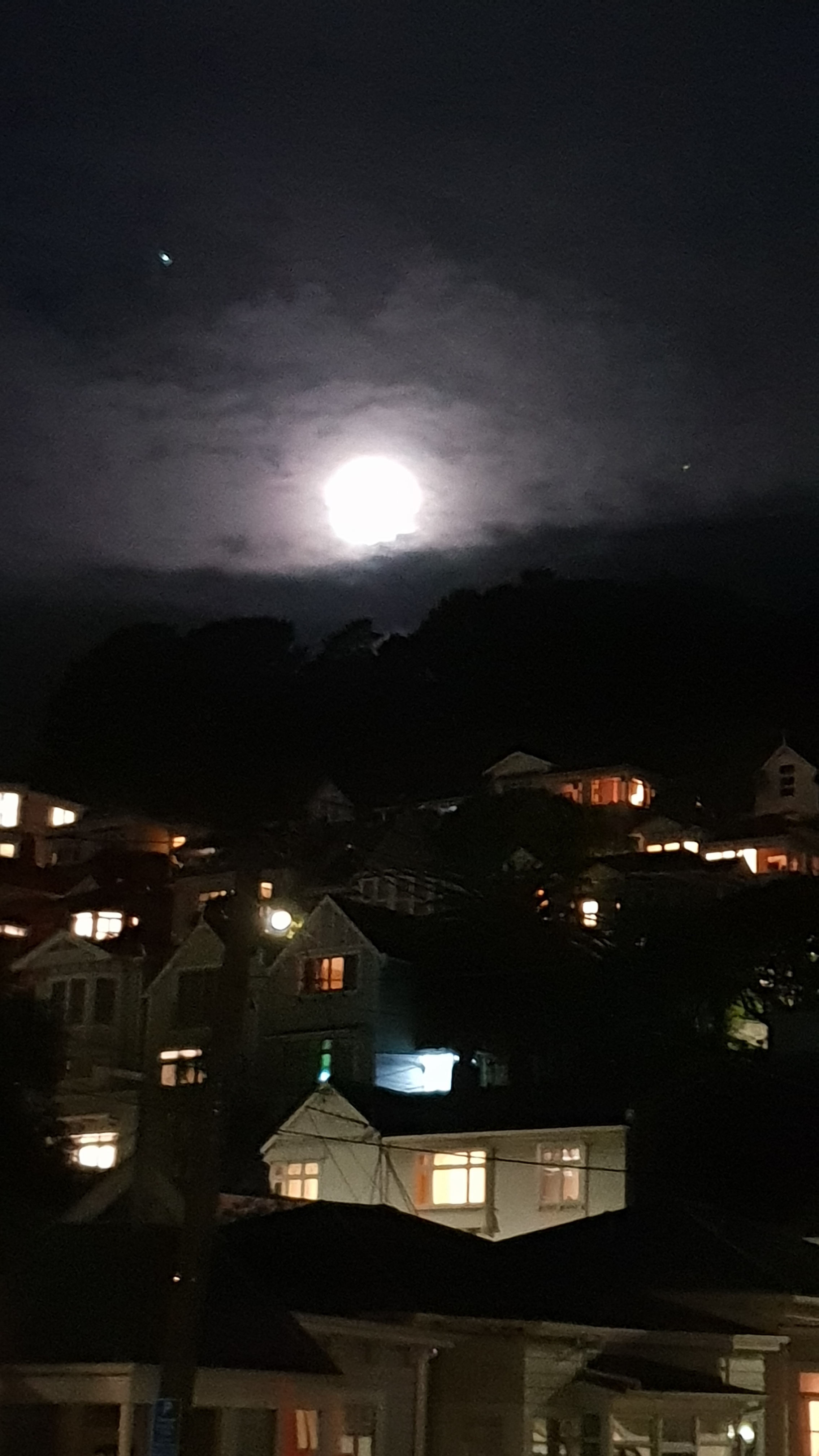 A full moon rising over the hills edge. The lights of houses fill the bottom of the scene