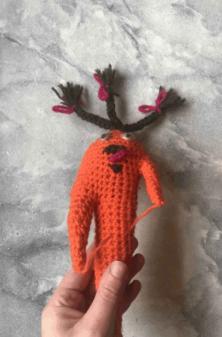 an angry crochet carrot is being tapped agressively on a marble surface by a human hand.