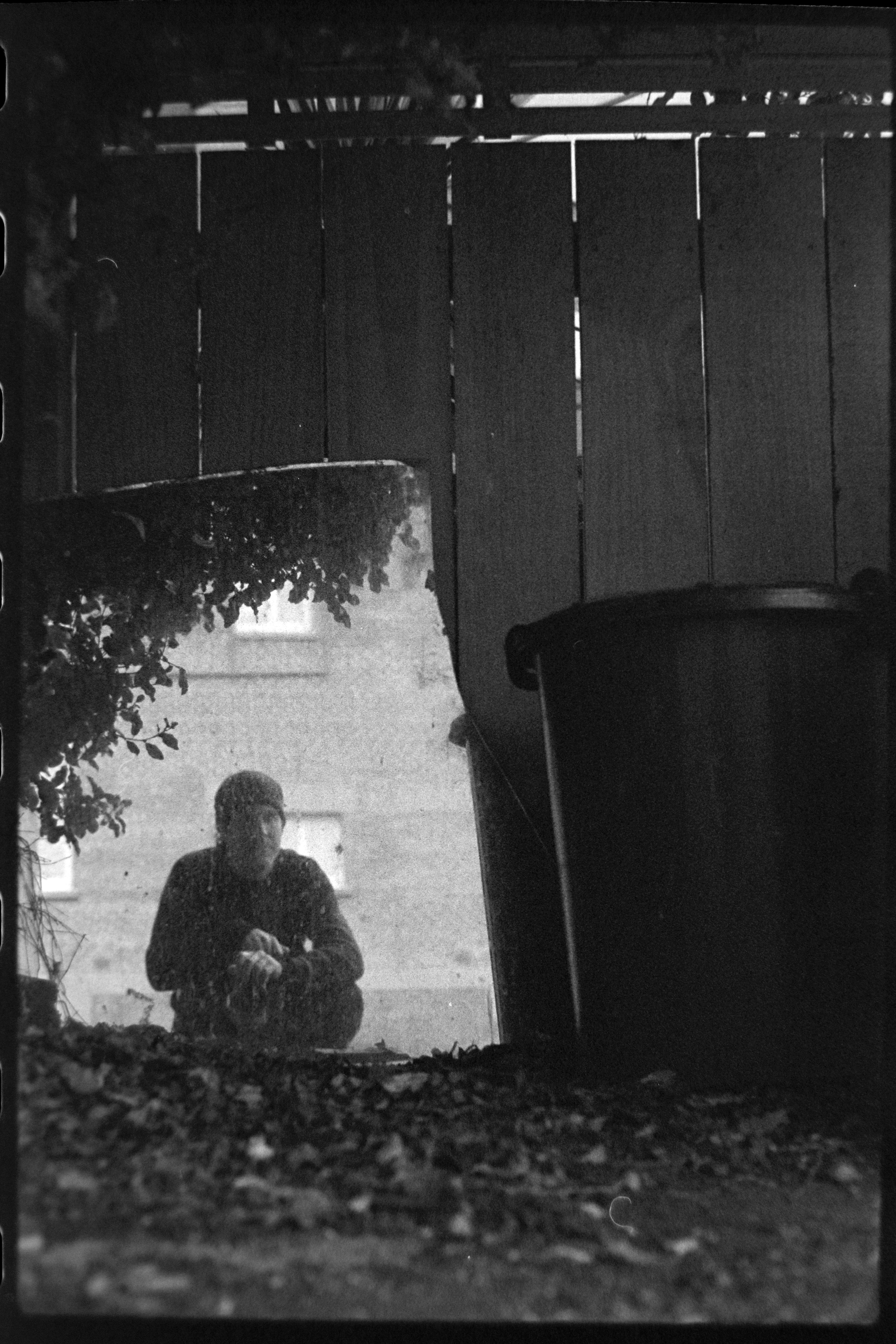 a self portrait of the photographer reflected in a mirror that is outside by some bins.