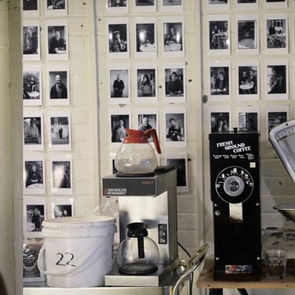 Many black and white potraits on a cafe wall with a jug of coffee in the foreground