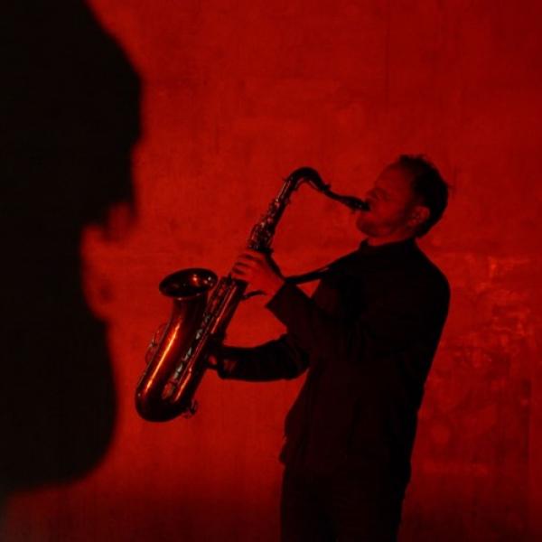 a red photo of Reuben holiding his saxophone out and up to blast the notes into the room