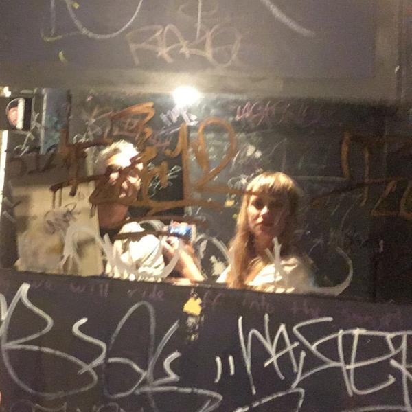 two people stand in front of a dirty graffiti-covered venue bathroom mirror taking a selfie
