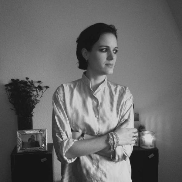 Gemma Thompson stands with her arms loosely folded. She is in thought