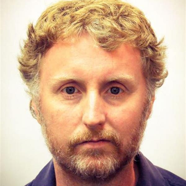 A stark headshot of Mark. He is in front of white wall. This could well be a passport photo.