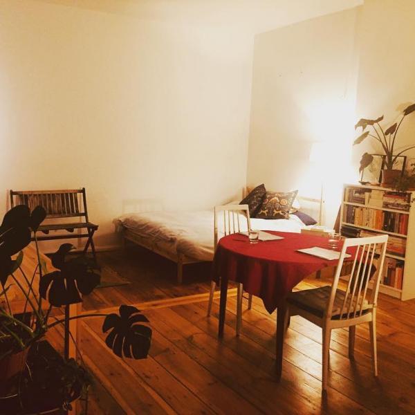 A very tidy bedroom. A table with a red table cloth. There are two glasses of water set on the table, two pads of paper, and two chairs.