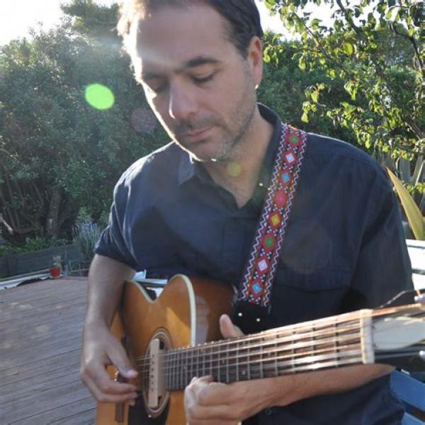 Joe playing an acoustic twelve string guitar. he looks calm and gently happy in  his endeavour.