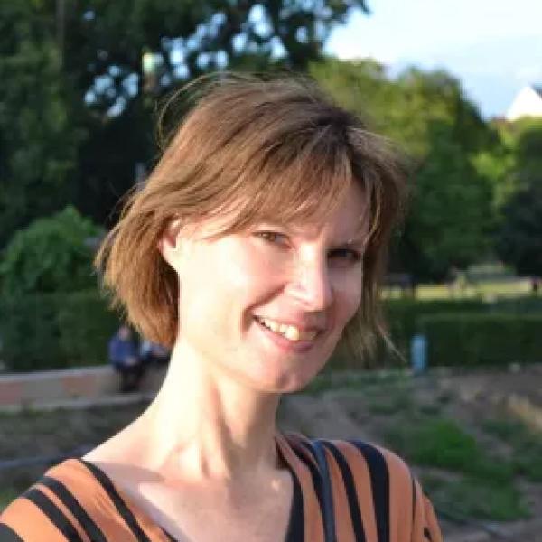Penny is smiling while standing in a large grassy and tree lined park