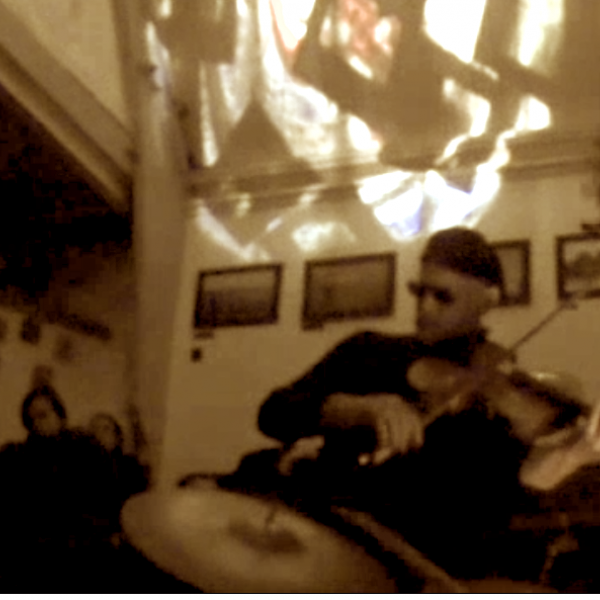 a very blurred photo of Peter playing viola. He is wearing dark sunglasses and a beret. There is a play of light on the ceiling.