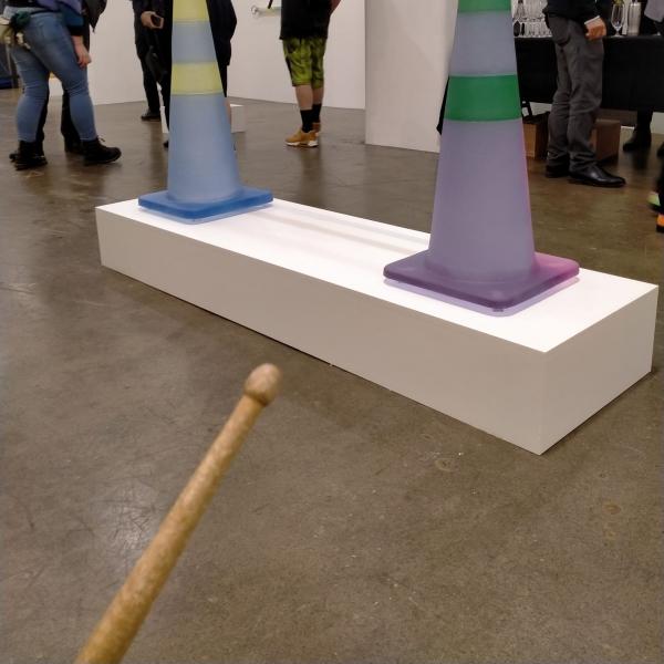 an image from a first person perspective; you are holding a drum stick and advancing towards two lilac coloured roadcones. You are in an art gallery