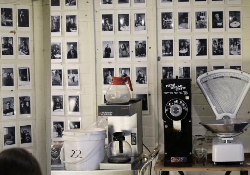 Many black and white potraits on a cafe wall with a jug of coffee in the foreground