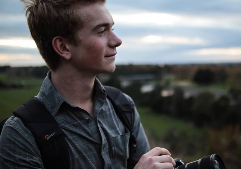 Charlie looking out from a low hill top. He is holding his camera down low as he gazes to the distance.