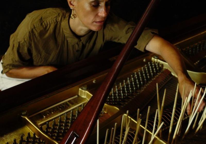 Hermione reaching into the innards of a grand piano. There are chopsticks thrust between the strings and standing upright.