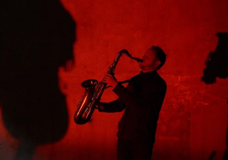 a red photo of Reuben holiding his saxophone out and up to blast the notes into the room