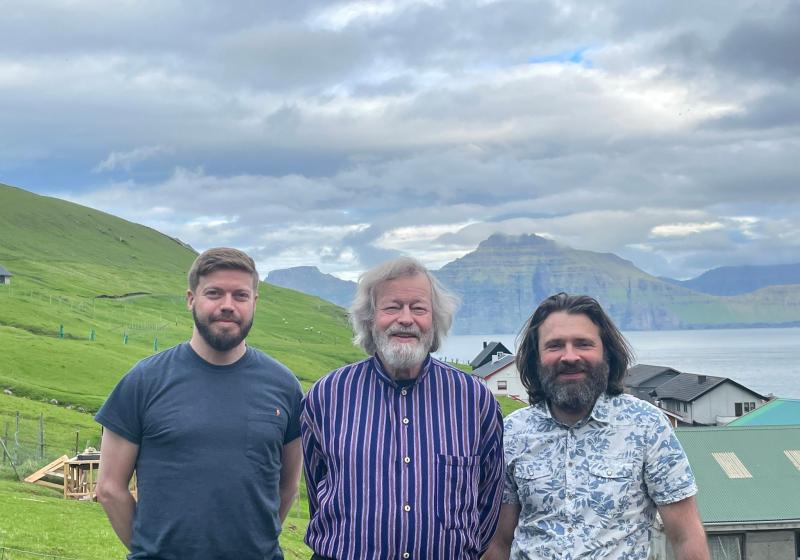 Three bearded men stand in the green jagged hills of the Faroe Islands