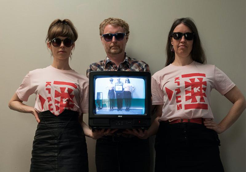 The three band members are looking cool in sunglasses, kraus t-shirts, and holding an old tv.