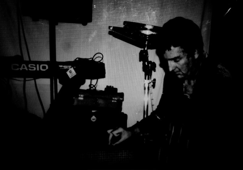 A very dark black and white photo of Peter. It looks like he may be playing a guitar on a table top.