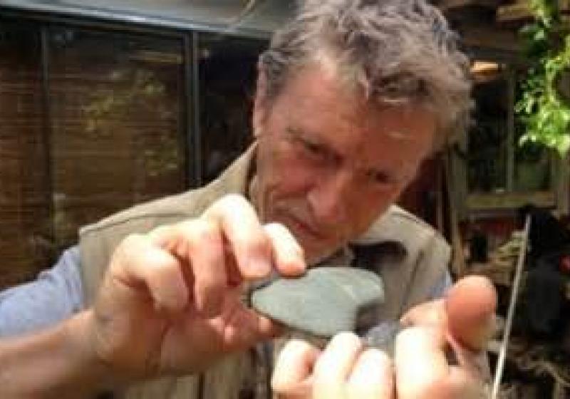 Phil is holding one rock in his cupped palm, in his other hand he is delicately holding a larage flat pebble. The pebble is held just above the rock. The look of concentration on Phil's face shows that he is in the middle of striking the two stones together as a musical sound