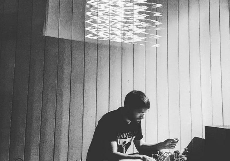 Felix playing modular synths in a black and white image, a wavey sculpture hangs in the room above him. 