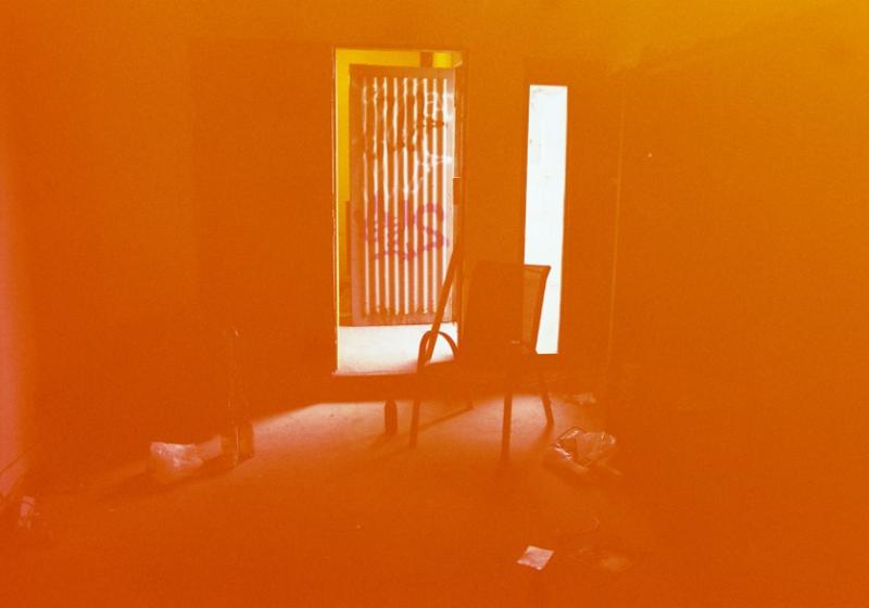 photo of a chair centred in a dark room with light reflecting from windows. photo is saturated in orange/red tones
