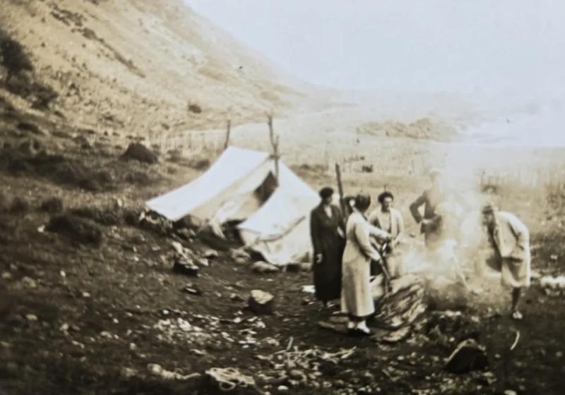 A sepia photo of people next to a tent in the mountains