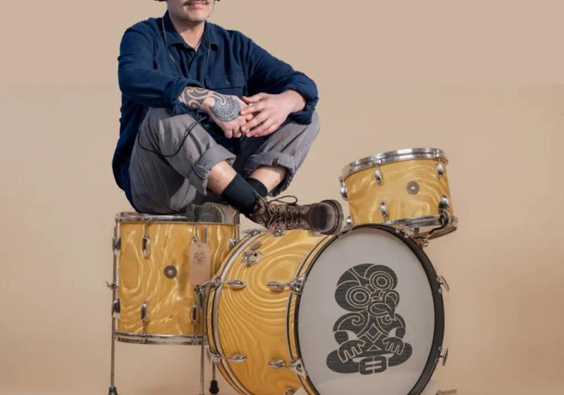 Riki Pirihi sits on a yellow drumkit with a blank background