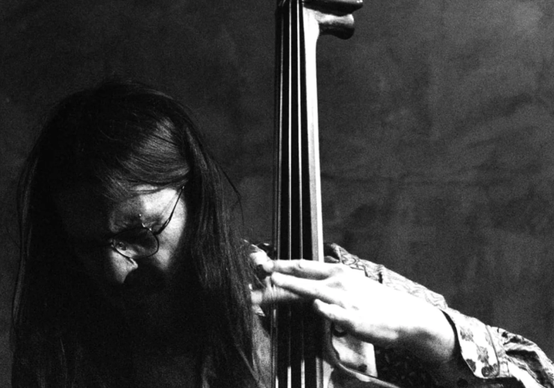 A moody black and white dim-lit photo of Arturo playing the double bass