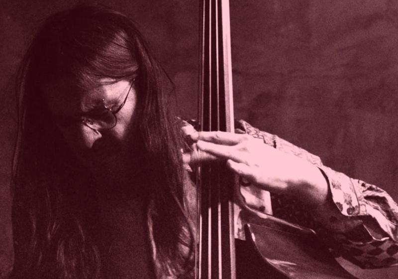 A moody black and white dim-lit photo of Arturo playing the double bass