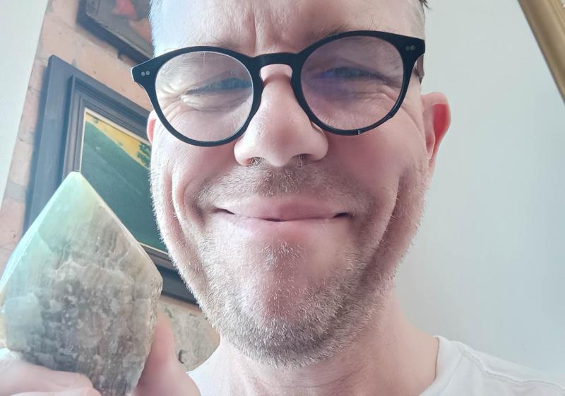 Chris smiles. His glasses are thick and dirty. He holds a crystal with pride