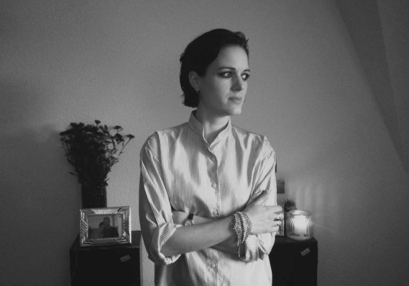 Gemma Thompson stands with her arms loosely folded. She is in thought