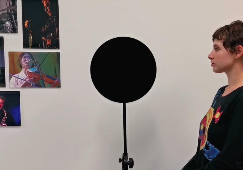 a black circle on a stand. A person stands next to it in profile