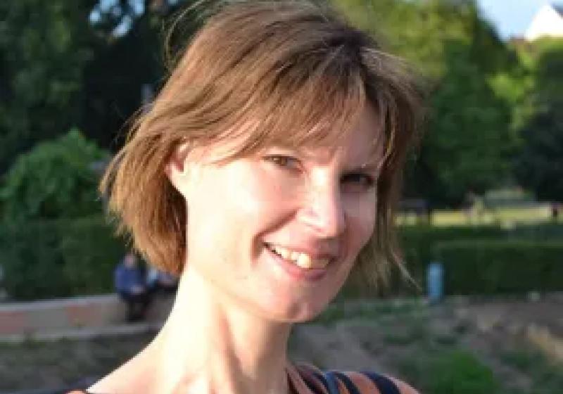 Penny is smiling while standing in a large grassy and tree lined park