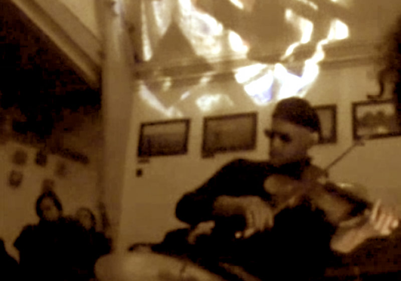 a very blurred photo of Peter playing viola. He is wearing dark sunglasses and a beret. There is a play of light on the ceiling.