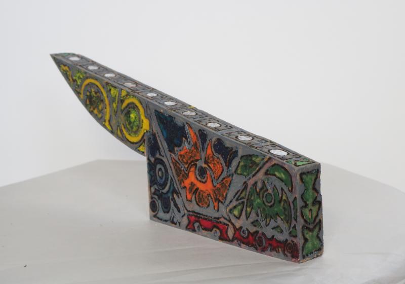 the cleaver is rough cut from wood. It is silver with abstract designs in yellow, orange, and green.
