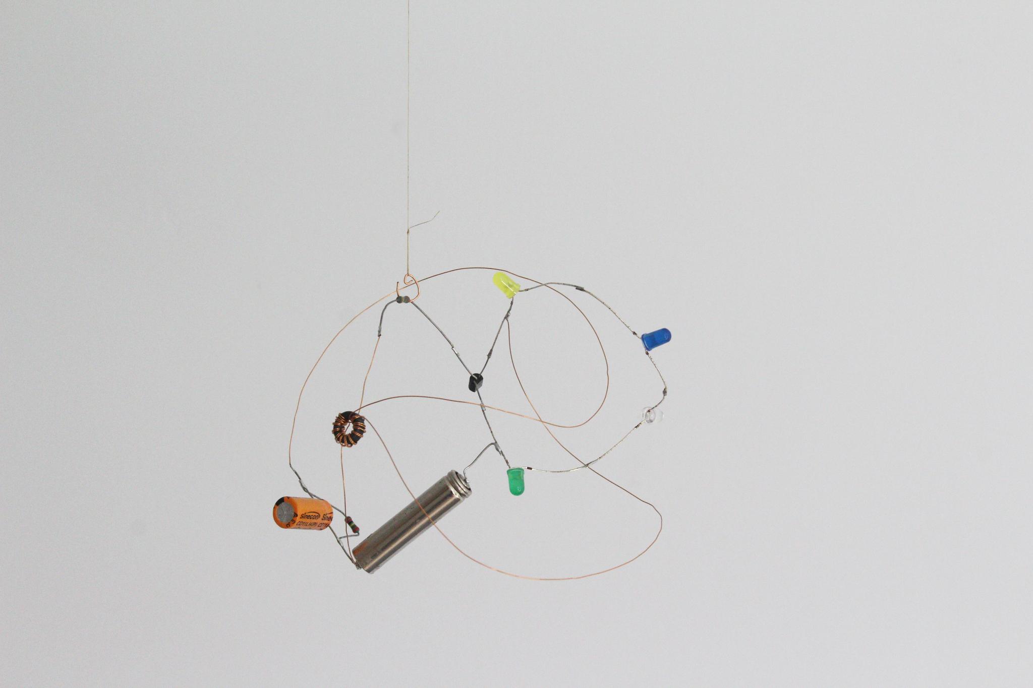 Free form Joule Thief circuit: Flat AAA battery, coloured LEDs, copper wire, hand wound coil on ferrite toroid, resistors, capacitor, transistor.