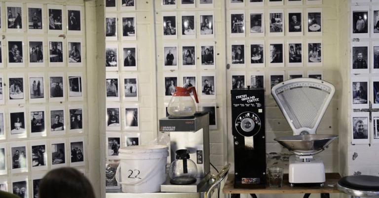 Many black and white potraits on a cafe wall with a jug of coffee in the foreground