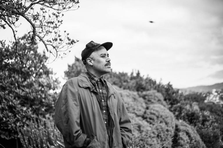 a black and whit portrait of Riki looking our over a block of bush.