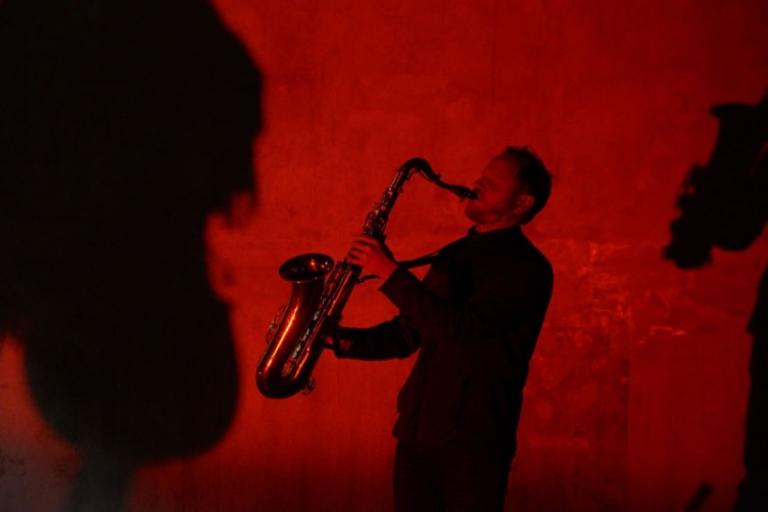 a red photo of Reuben holiding his saxophone out and up to blast the notes into the room
