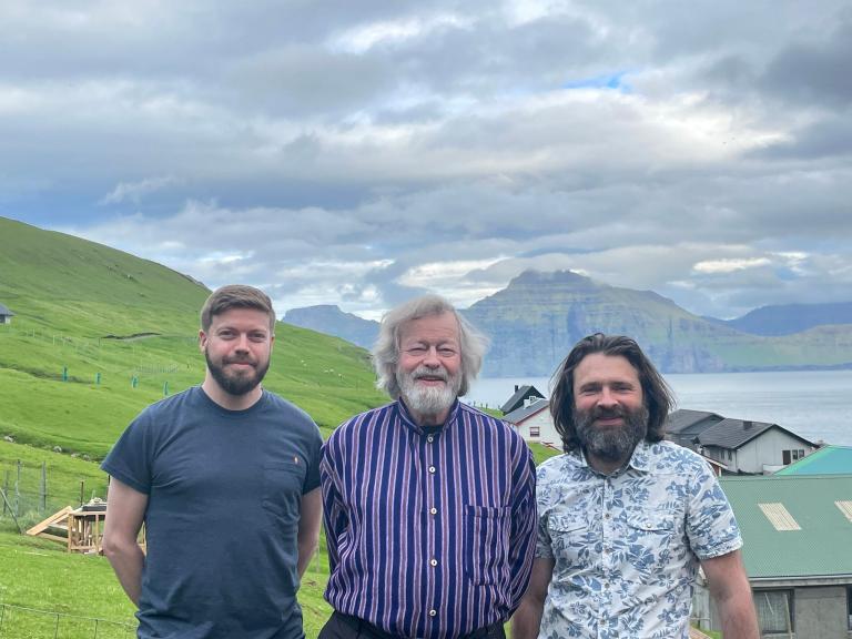 Three bearded men stand in the green jagged hills of the Faroe Islands