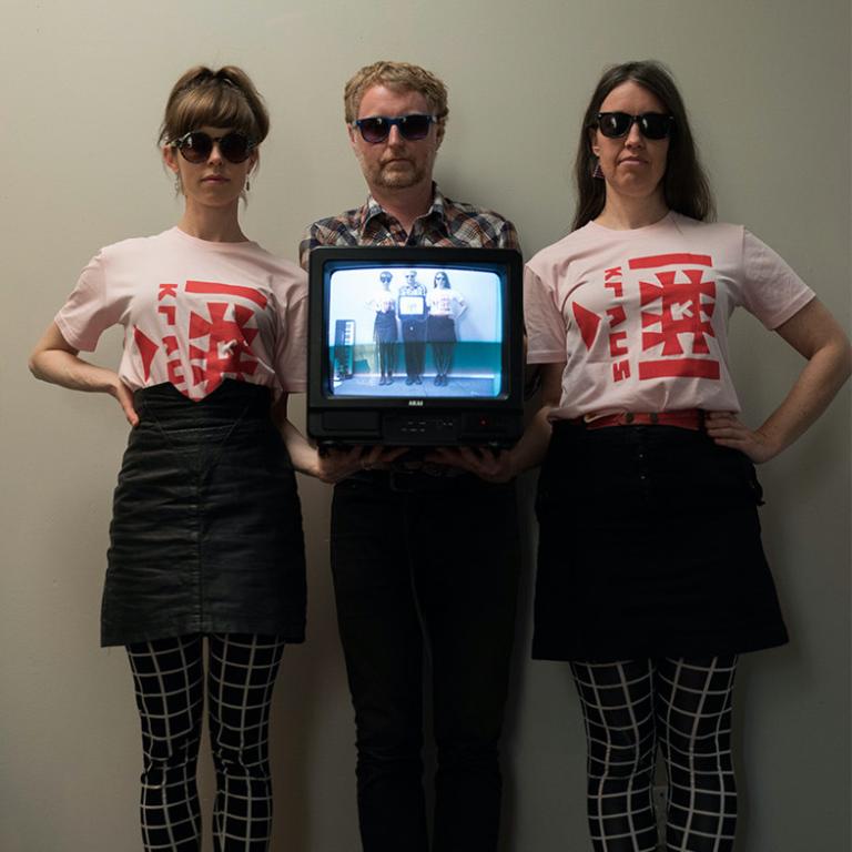 The three band members are looking cool in sunglasses, kraus t-shirts, and holding an old tv.