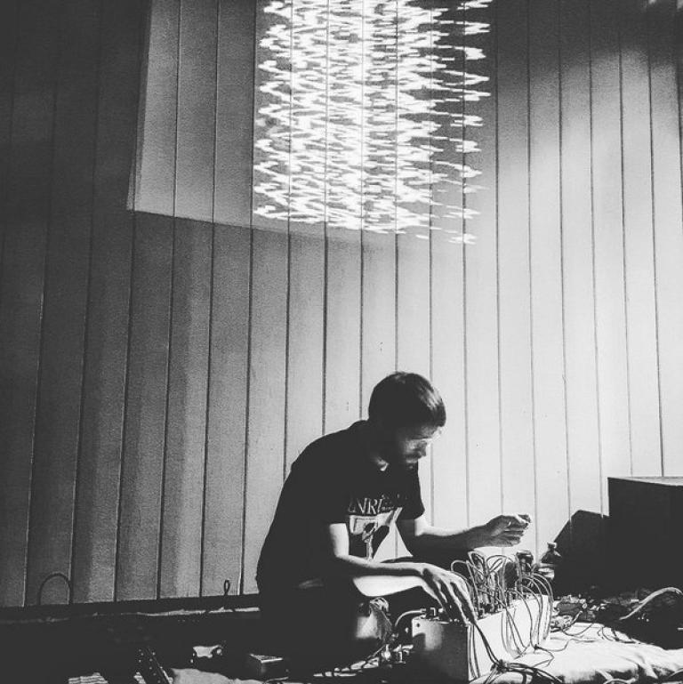 Felix playing modular synths in a black and white image, a wavey sculpture hangs in the room above him. 