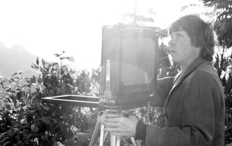 Andrew Ross stands next to a fold-out accordion-style camera, taking a long exposure photograph in the sun.