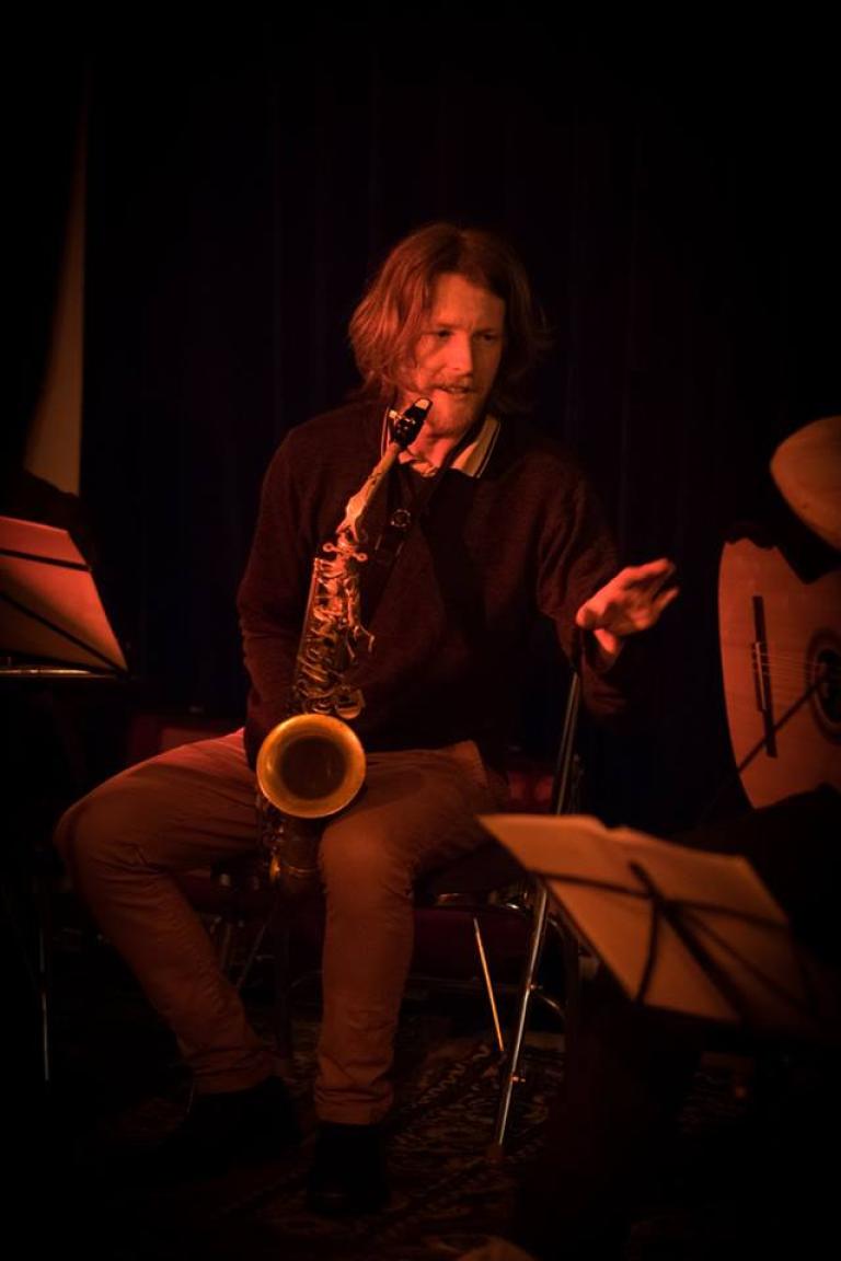 Glen Downie appears under red light with his alto saxophone