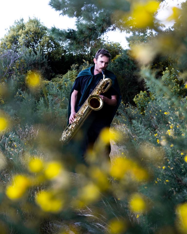 Jake Baxendale playing the saxophone in a bush 