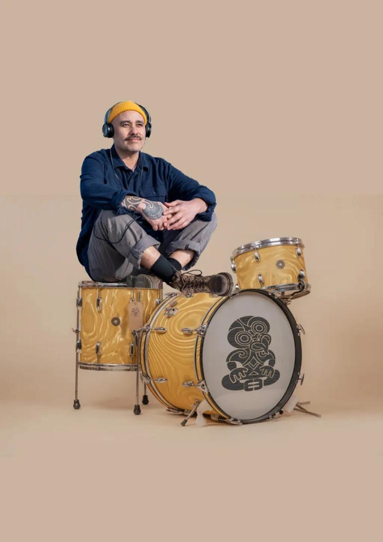 Riki Pirihi sits on a yellow drumkit with a blank background