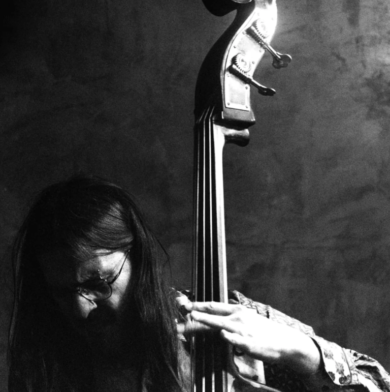 A moody black and white dim-lit photo of Arturo playing the double bass